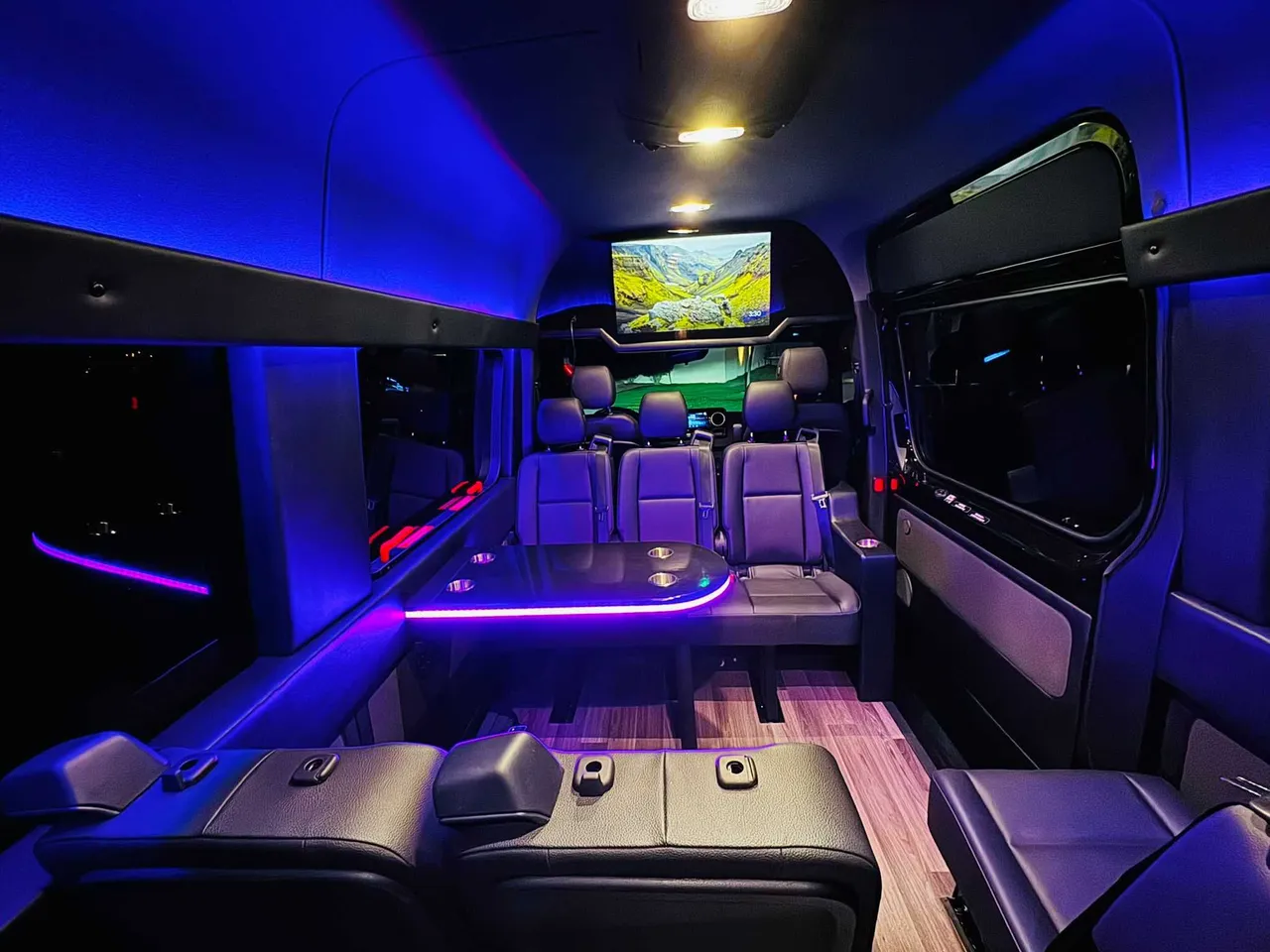 Mercedes-Benz Executive Sprinter for party bus rental: seating area, with passenger tables, LED accent lighting and wood-look flooring, pic 3